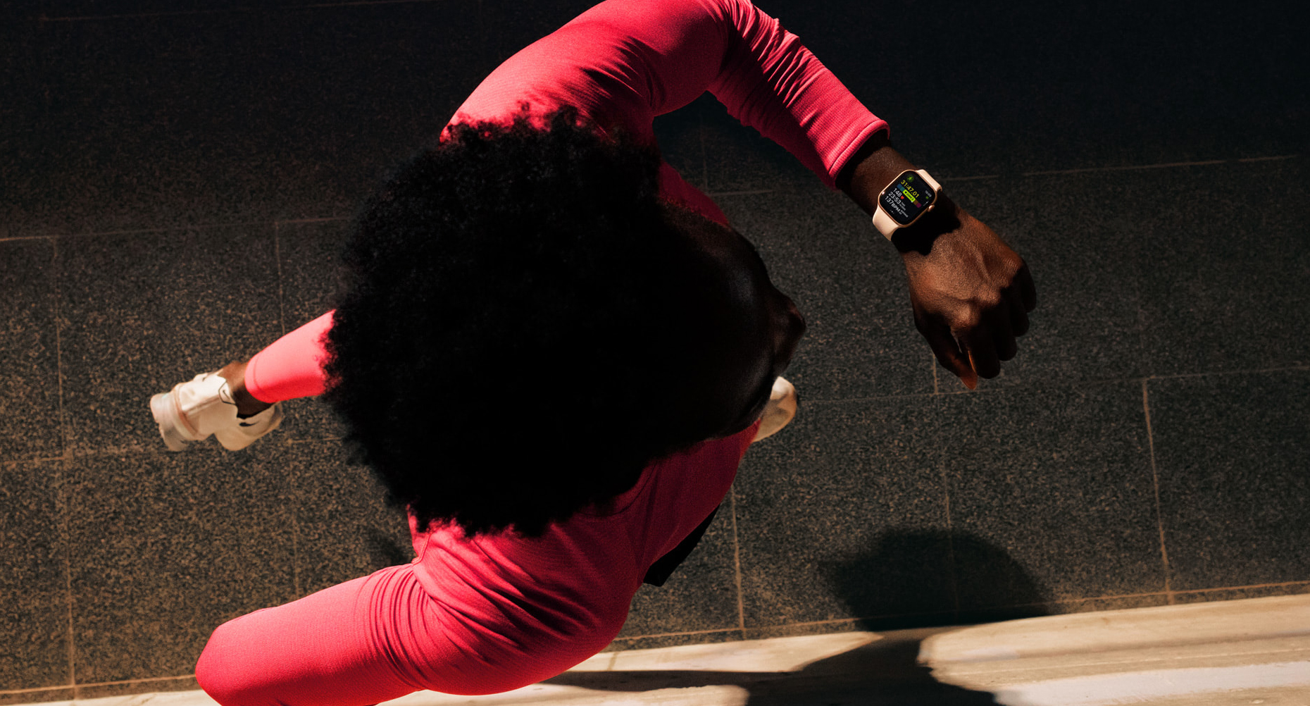 Человек бежит по темной улице, глядя на свои Apple Watch, на которых отображается приложение Workout Buddy.